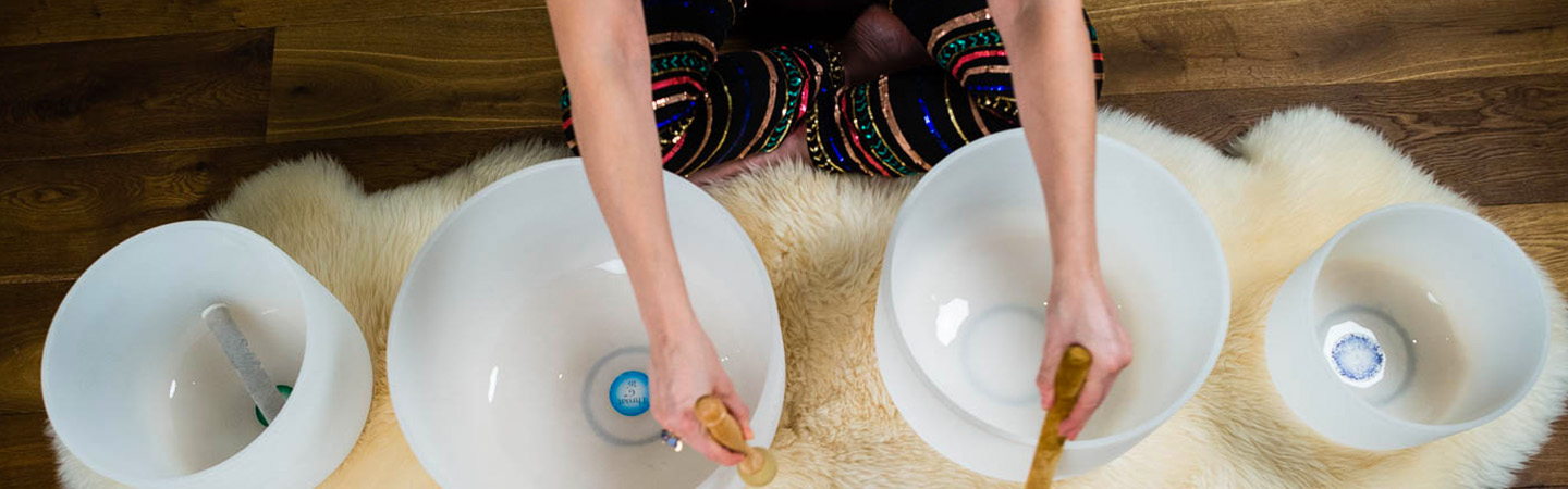 Overhead image of a person playing large crystal bowls with mallet strikers.