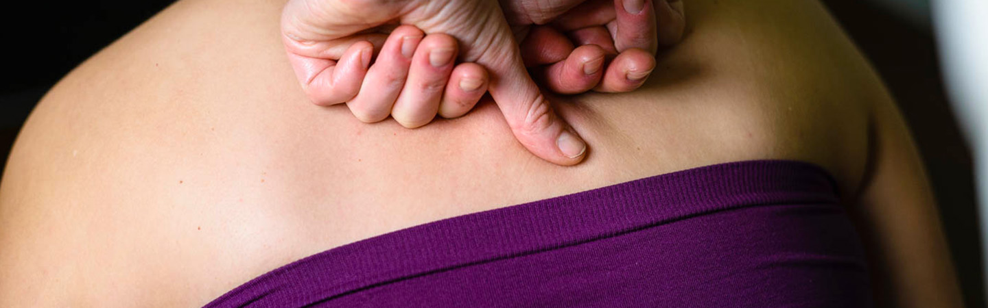 Image of two hands kneading the back of someone using massage technique.